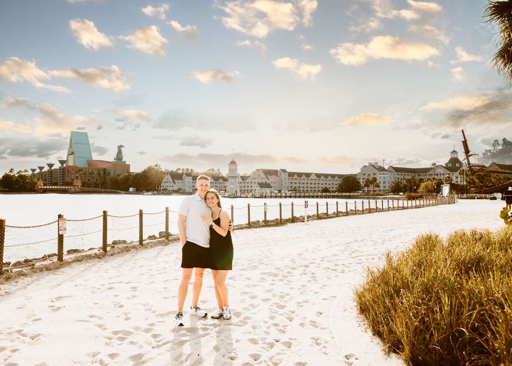 Young couple smiling at Disney Boardwalk sandy beach during sunset at urprise proposal. Cred: LexTakePix
