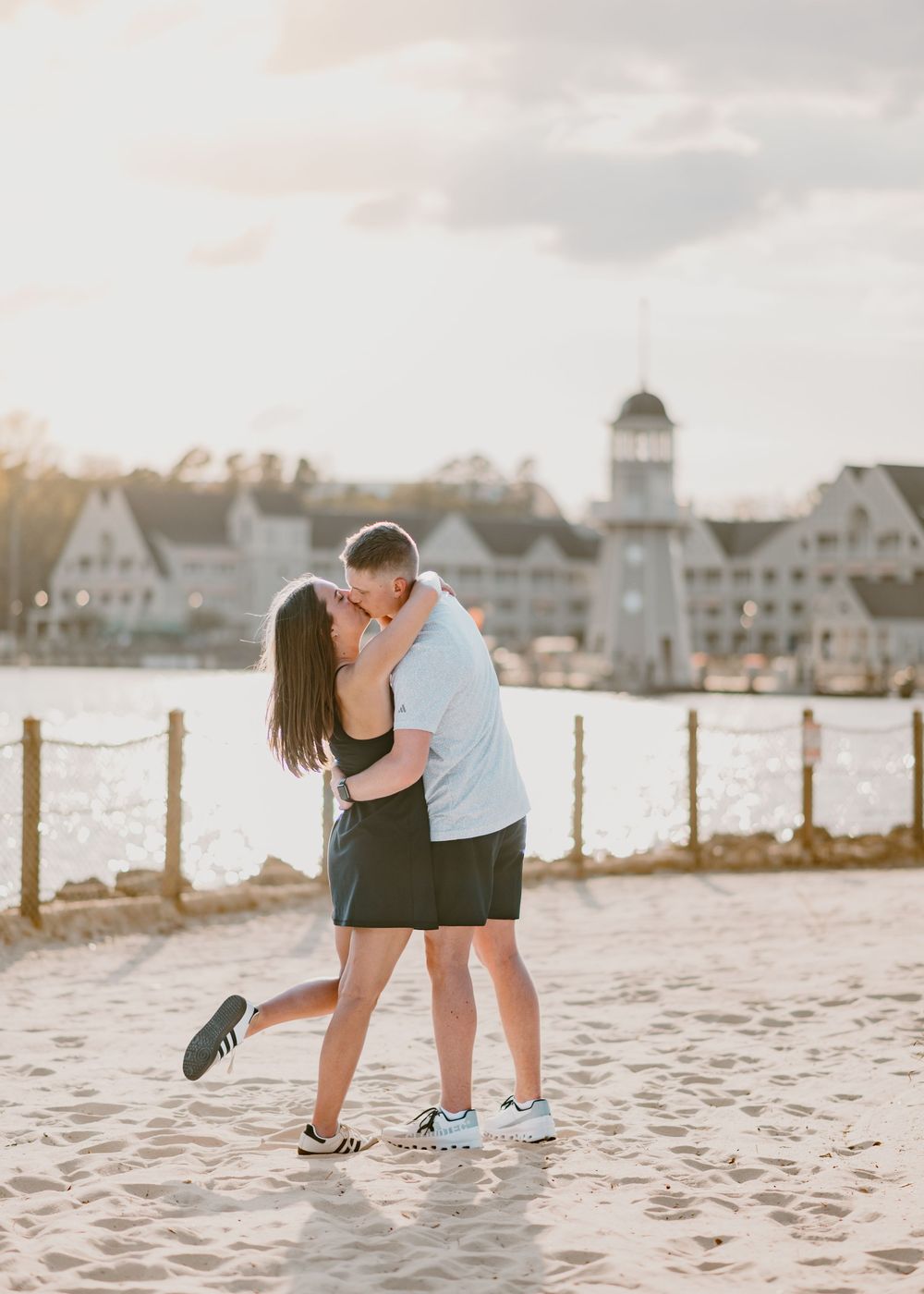 Young couple kissing at Disney Boardwalk sandy beach during sunset at urprise proposal. Cred: LexTakePix