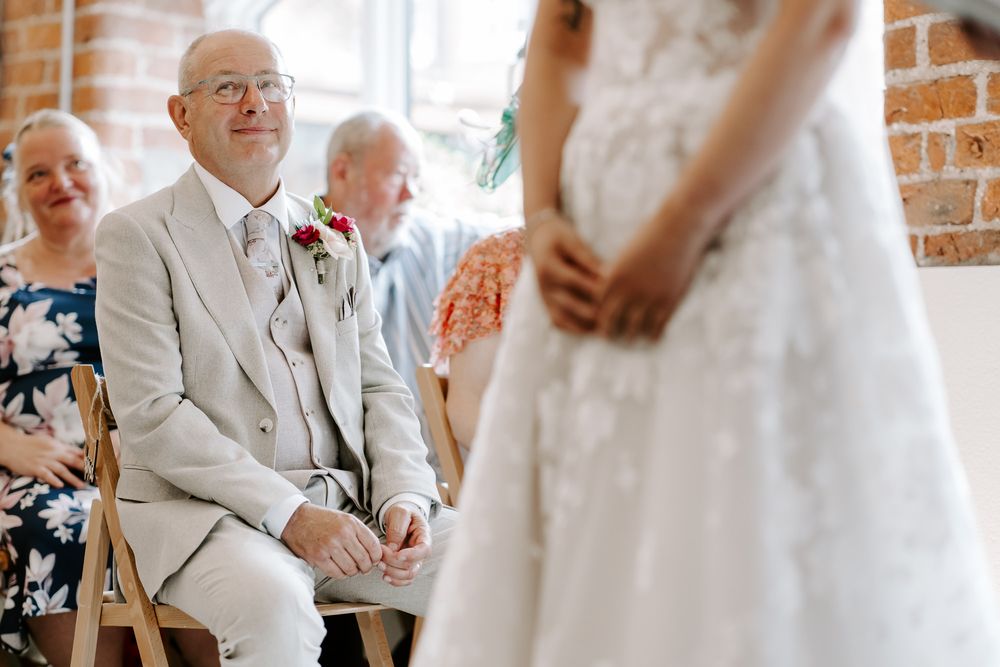 Wedding guests in white suit and dress share a candid moment of joy and laughter at an indoor reception venue.