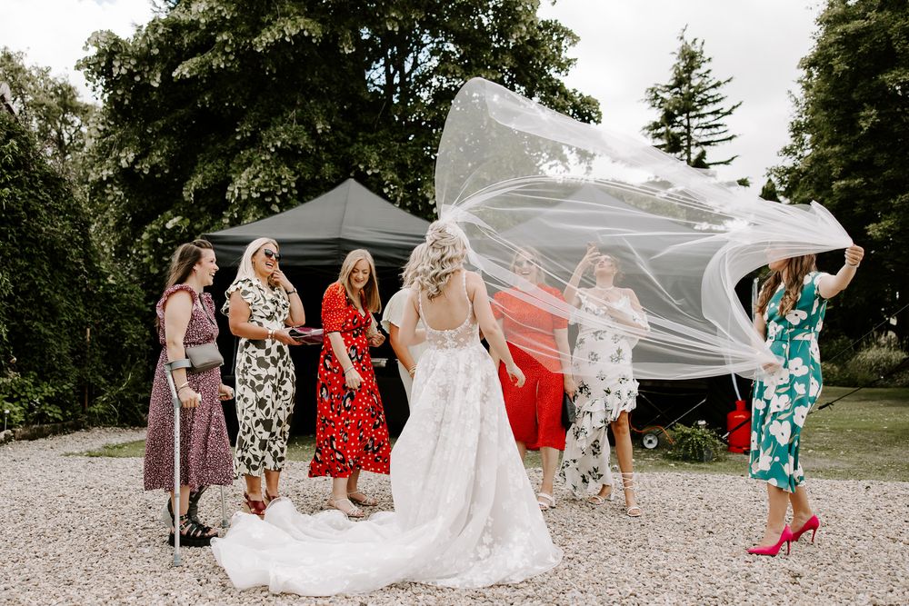 A candid series of people outdoors helping with a white wedding dress in a garden setting.