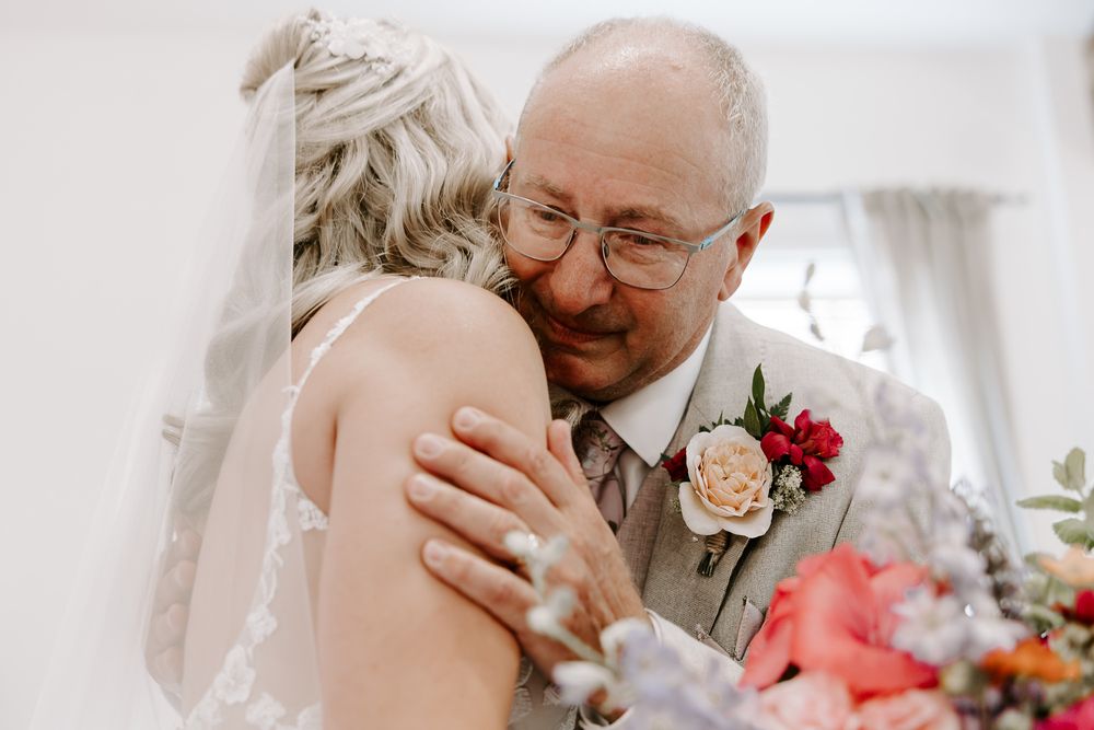 A tender wedding moment captured during a sunny outdoor ceremony with floral decorations and soft light.