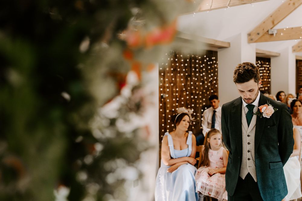 Indoor wedding ceremony scene with decorative string lights and formal attire against a white wall.