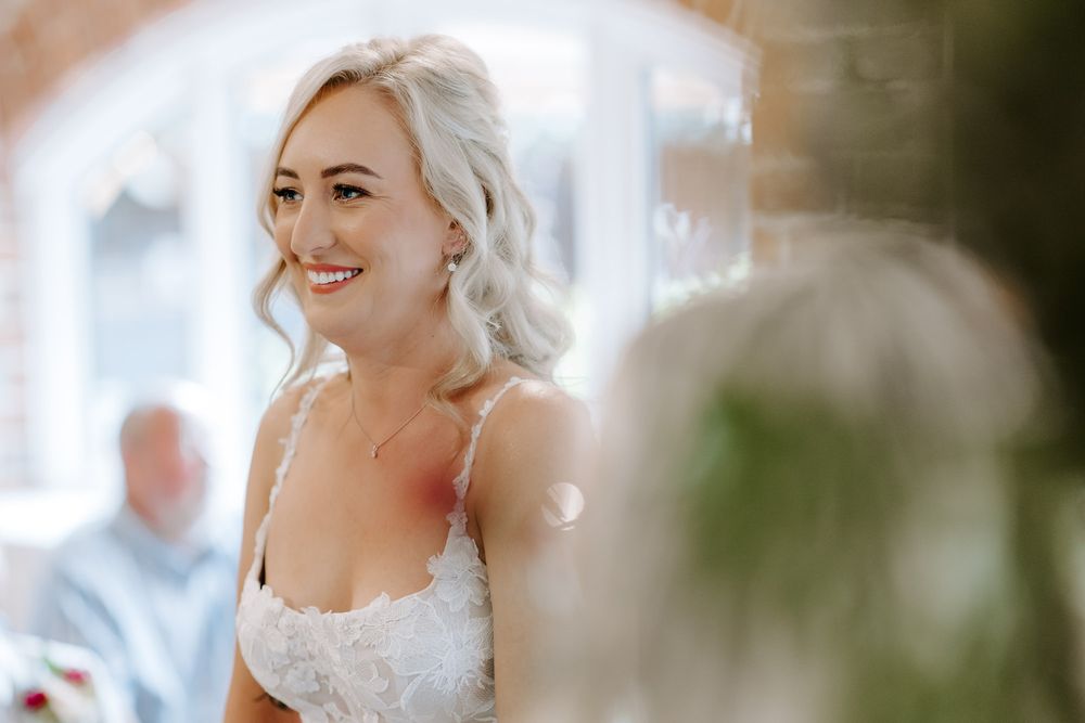 A close-up portrait of someone in a white lace wedding dress with soft lighting and greenery in the background.
