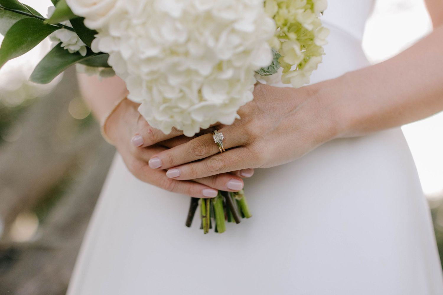 Close-up of hands holding white wedding bouquet showing wedding rings.