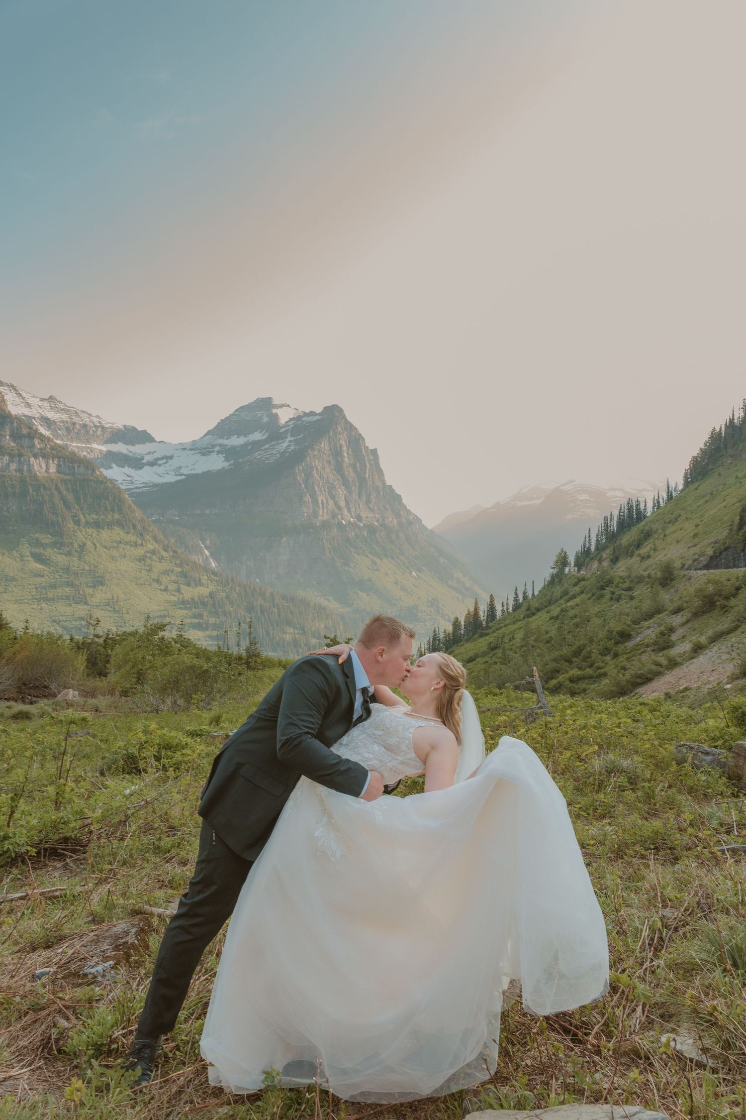 A romantic wedding couple shares a tender moment against the majestic backdrop of snow-capped mountains in Glacier National Park.