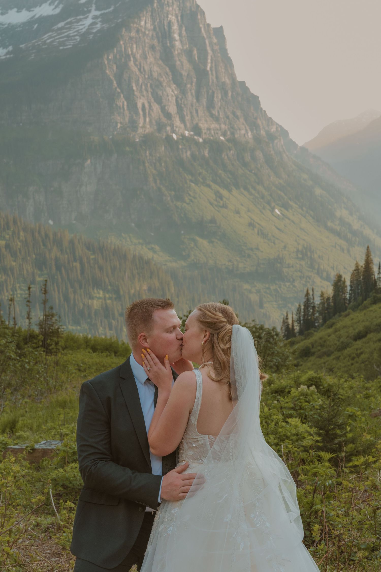 A couple shares a romantic kiss against a stunning mountain backdrop in Glacier National Park.