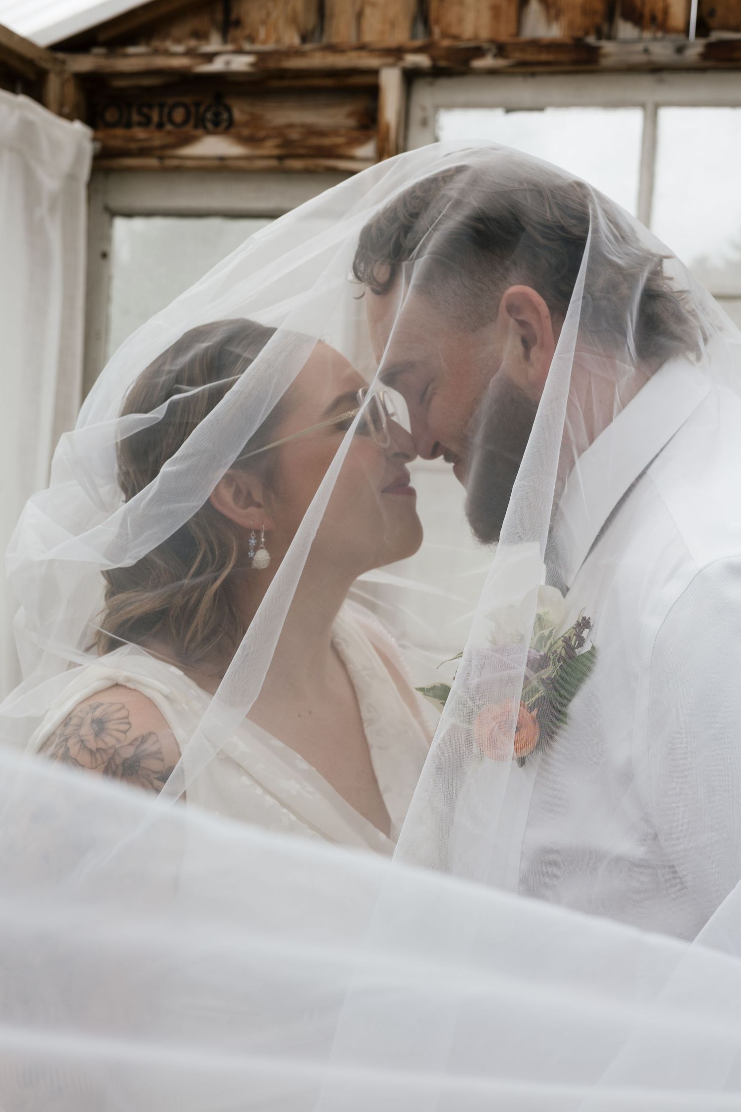 A romantic wedding moment under a sheer white veil as newlyweds share an intimate close-up embrace.