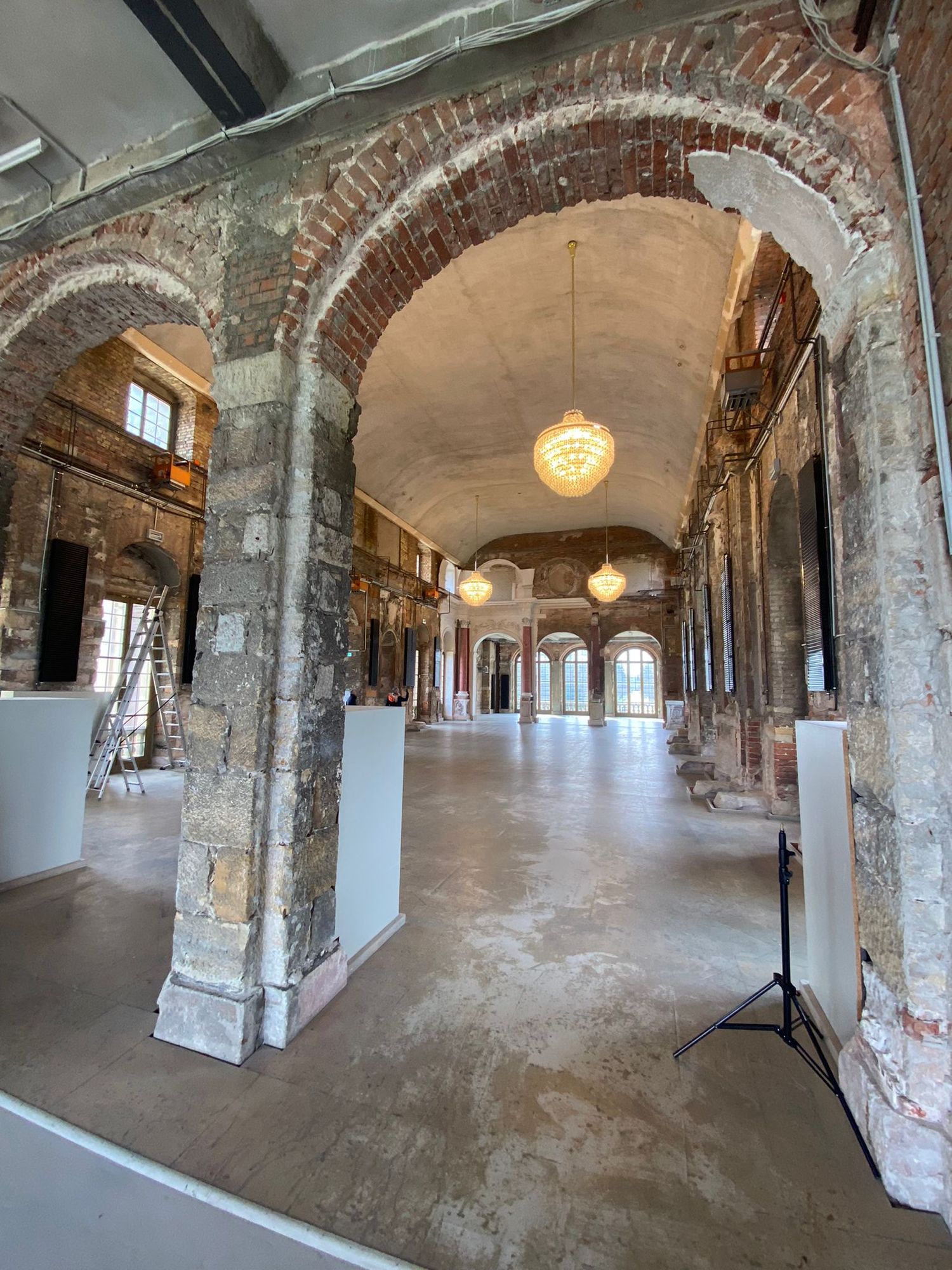 Rustic brick arches line a historic hallway with exposed architectural details, pendant lights, and concrete floors.