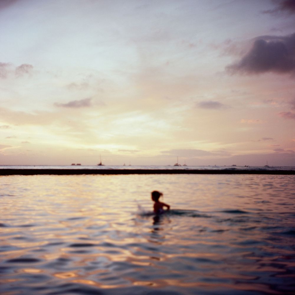 A silhouette in calm waters during sunset with boats on the horizon creating a tranquil seascape.