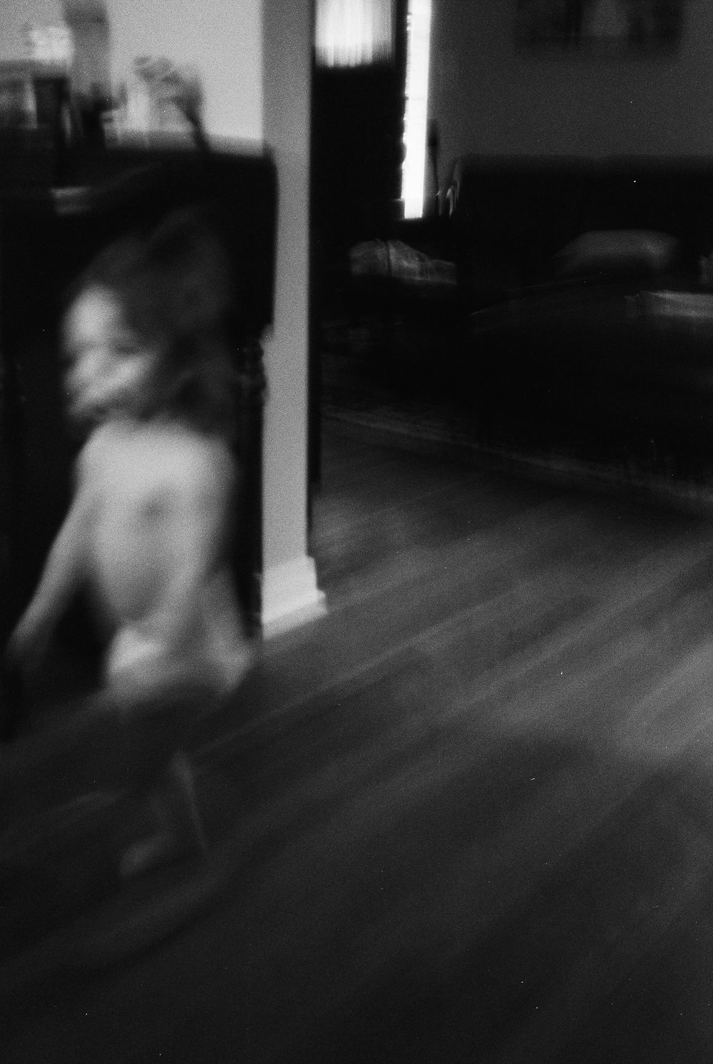 A sequence of blurry black and white security camera stills showing movement across a dark room with wooden floors.
