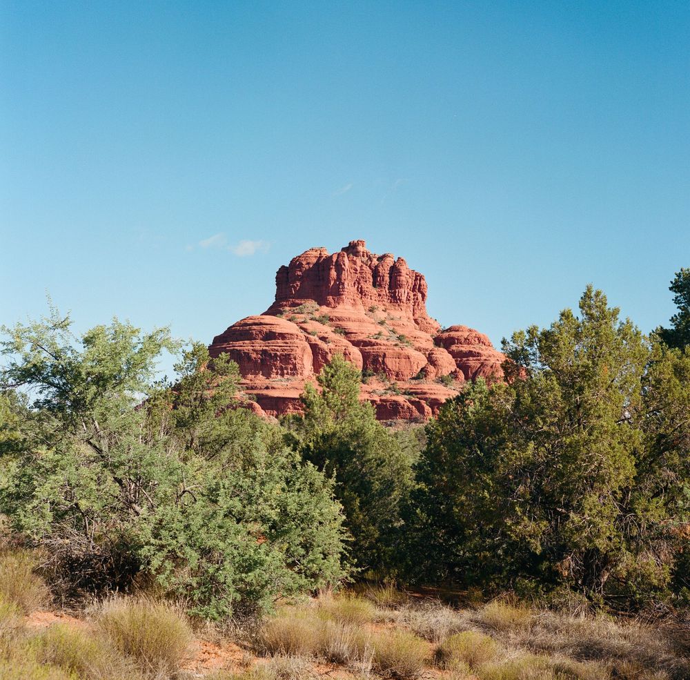 Scenic view of Bell Rock in Sedona Arizona with red sandstone formations and desert vegetation against blue sky.