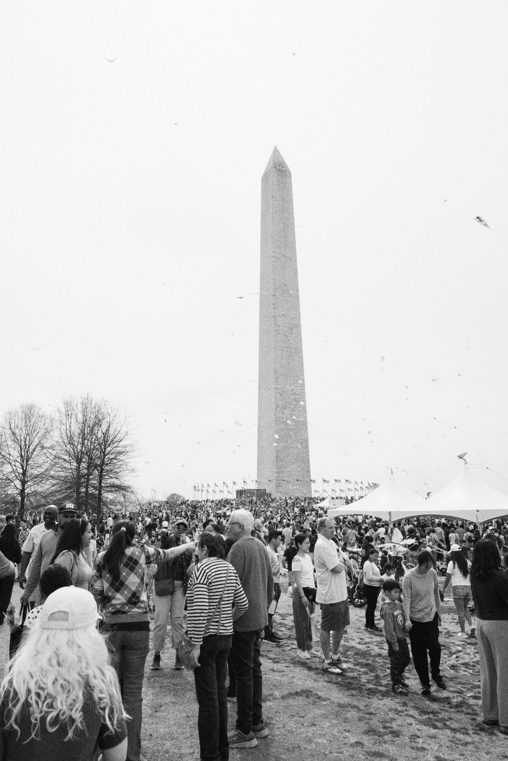 A large crowd gathers around the Washington Monument on a cloudy day in this black and white photograph.
