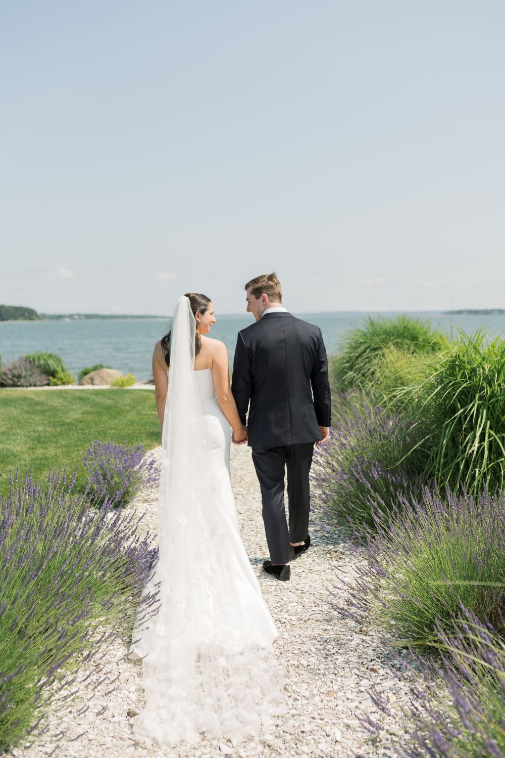 Wedding couple walking along a coastal path bordered by lavender and sea grass.