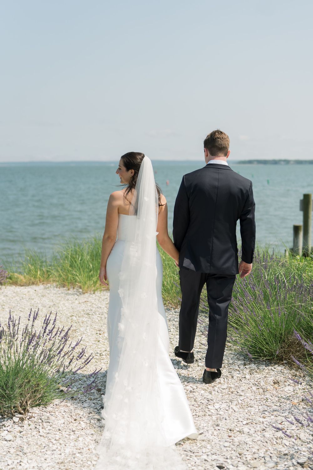 Elegant seaside wedding photo with a couple standing on a shell-lined path.