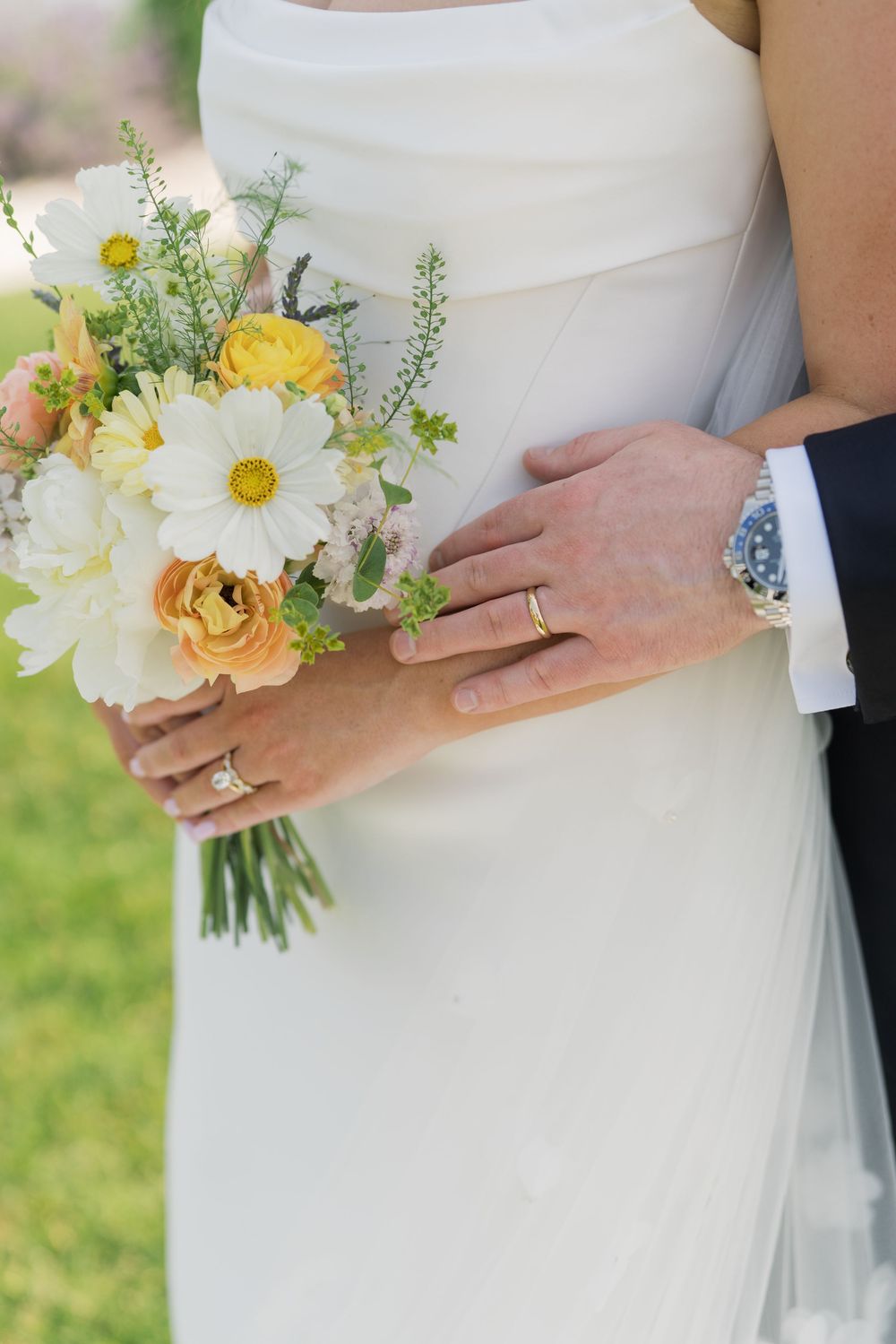 Wedding bouquet with yellow and white flowers held against white dress.