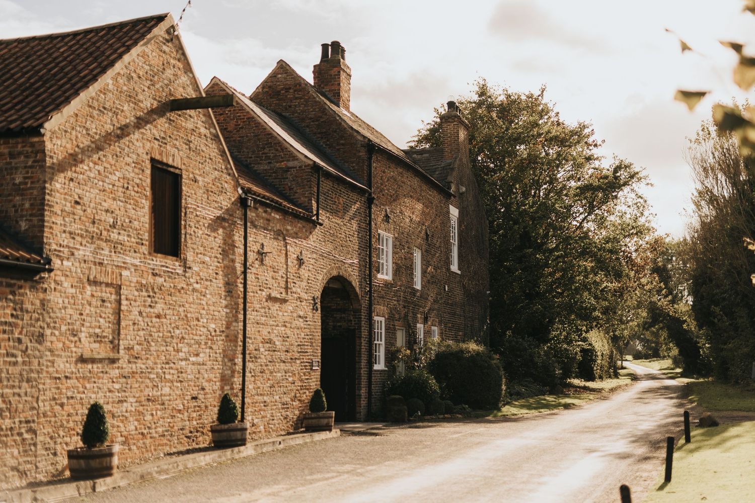 Historic brick buildings line a winding country road in a rustic rural setting during autumn.