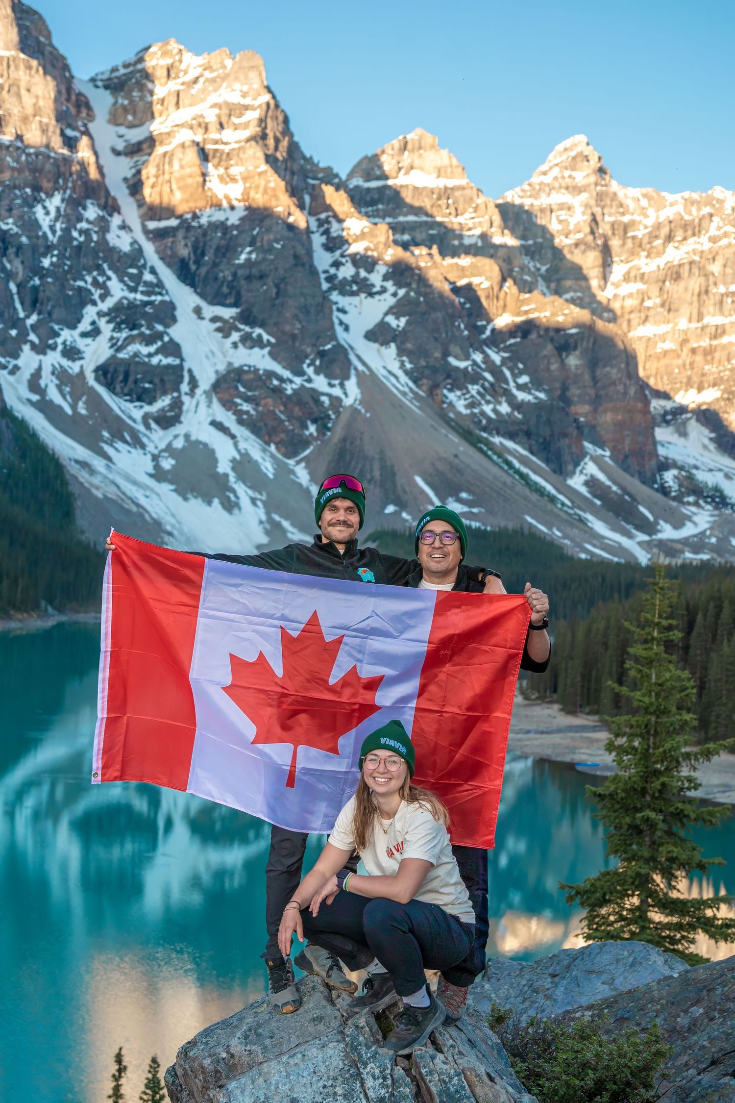 Tourists display Canadian flag against turquoise Moraine Lake and snow-capped Rocky Mountains in Banff National Park, Alberta.