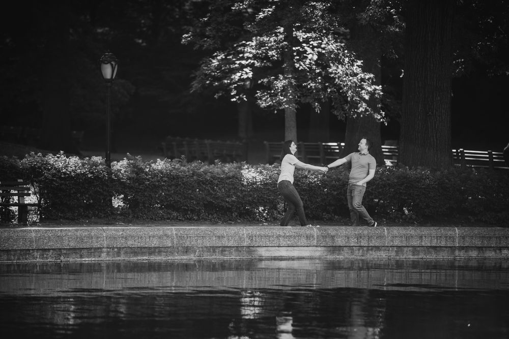 A couple dancing playfully by a reflecting pool in black and white photography.