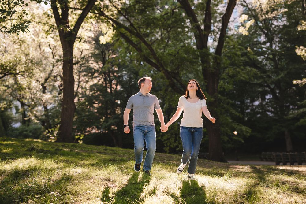 A couple walking hand in hand through a sunlit park with golden light filtering through trees.
