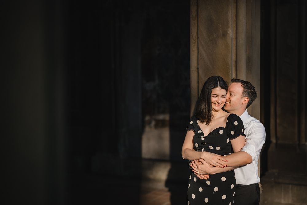 A romantic engagement photoshoot in a dark archway with dramatic lighting and shadows.
