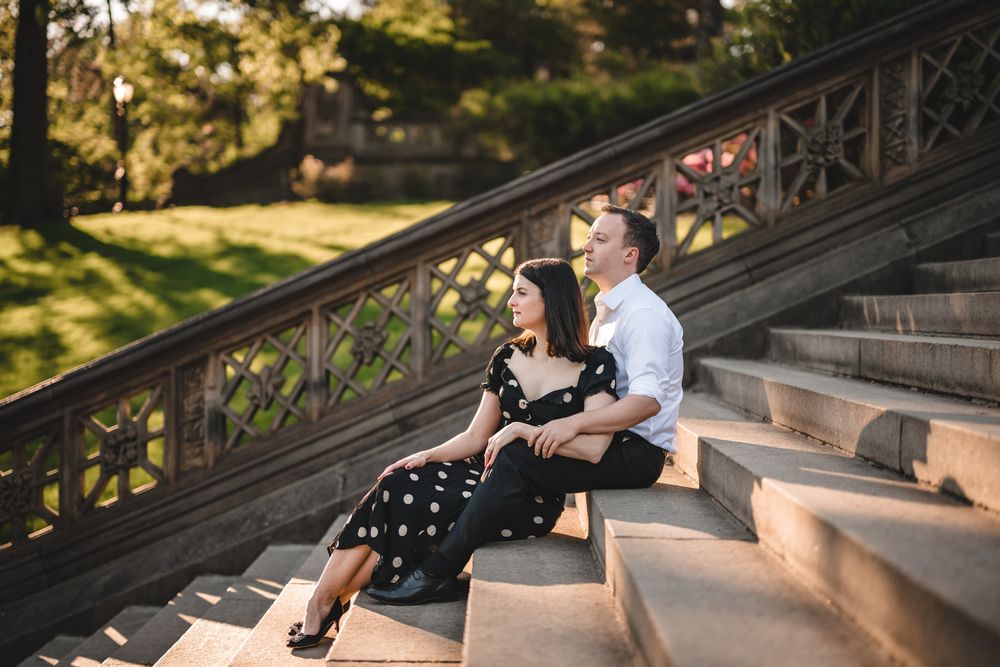 Couple posing together on stone steps in a sunlit outdoor setting.