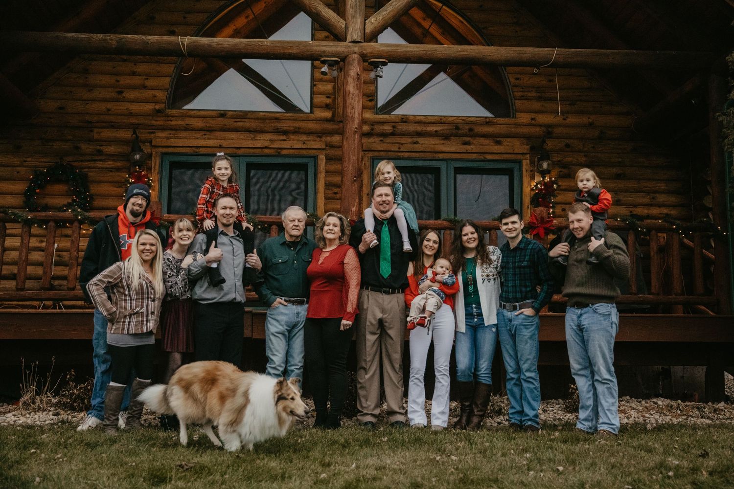 Large group poses in front of a rustic log cabin during a family gathering.