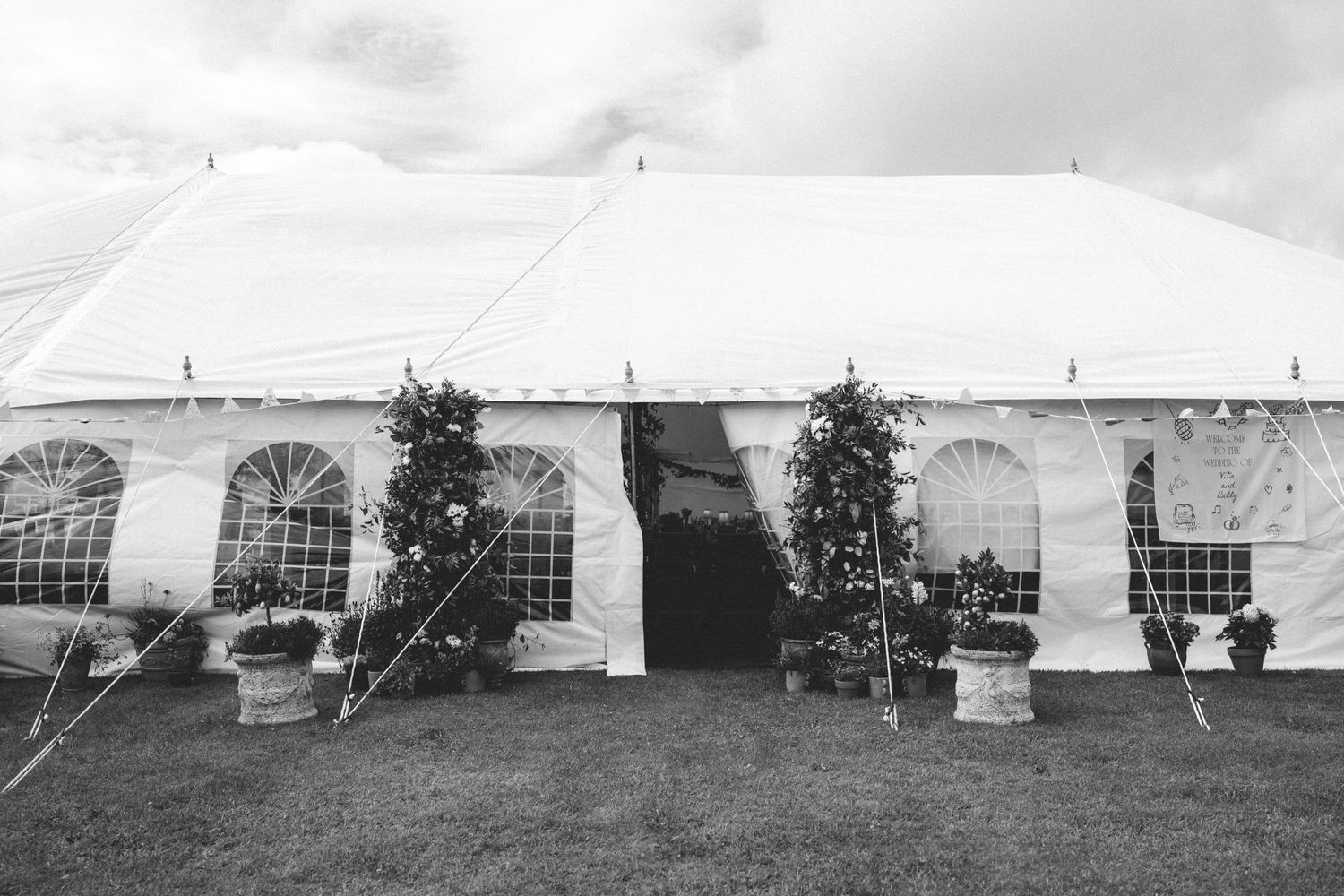 Five vintage white military tents spread across a field with dark silhouettes of trees visible against a cloudy sky.