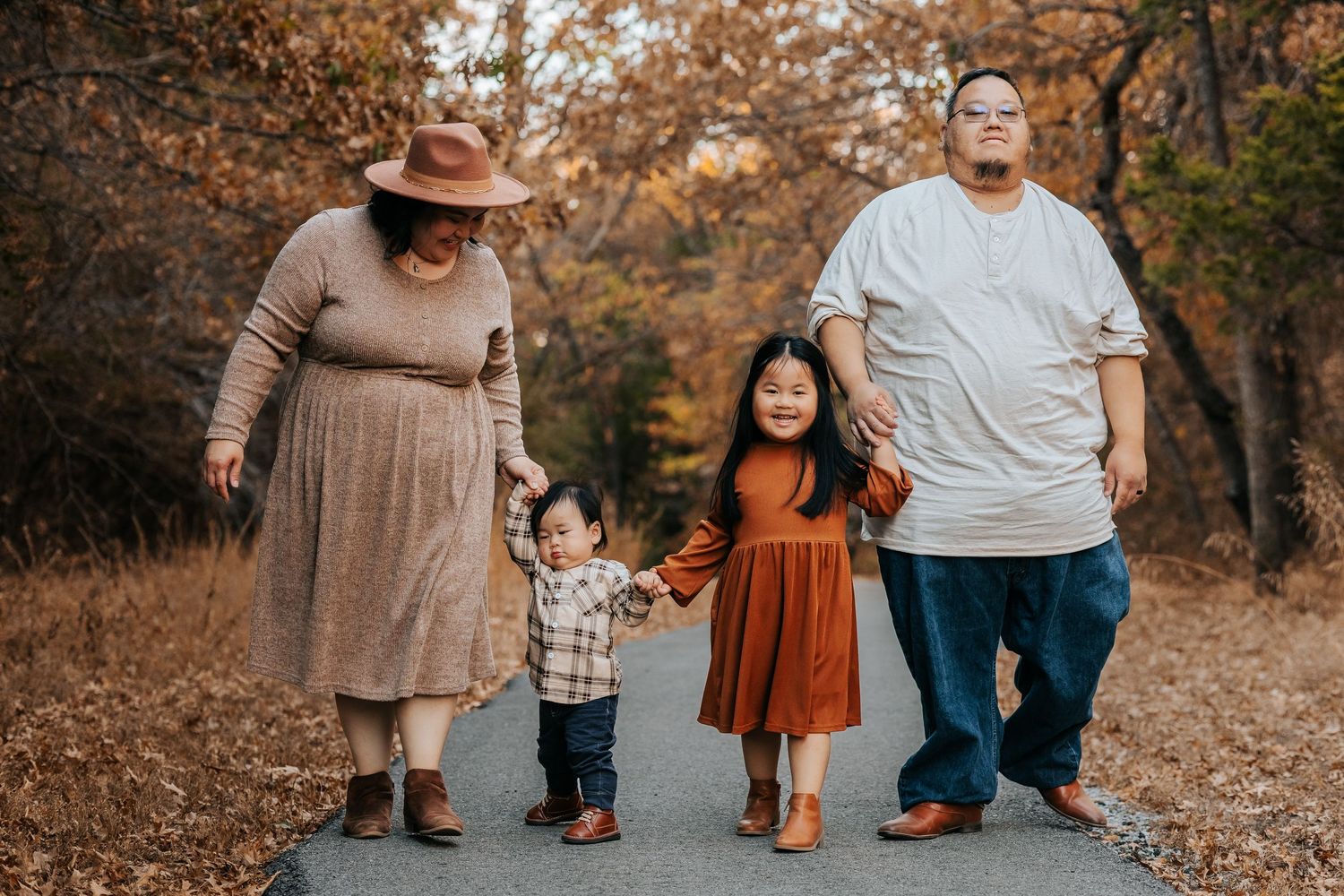 Family walking together on autumn path with fall foliage in background.
