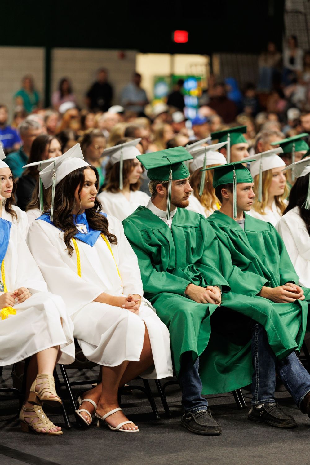 Graduates in white and green caps and gowns sit together during a commencement ceremony.