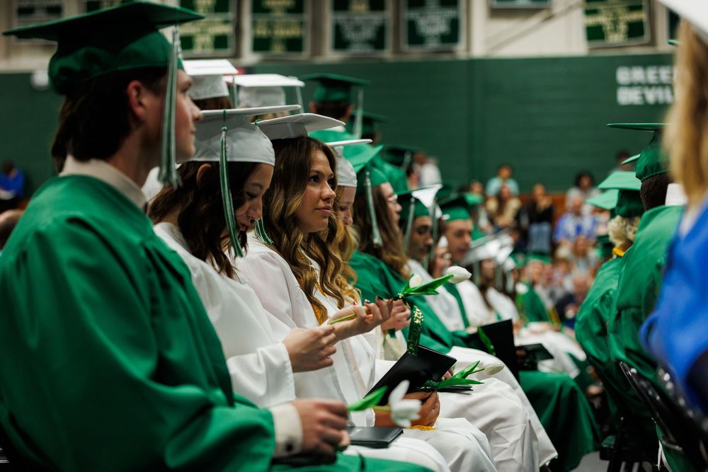 Graduates in green and white gowns sit in rows during a university commencement ceremony.