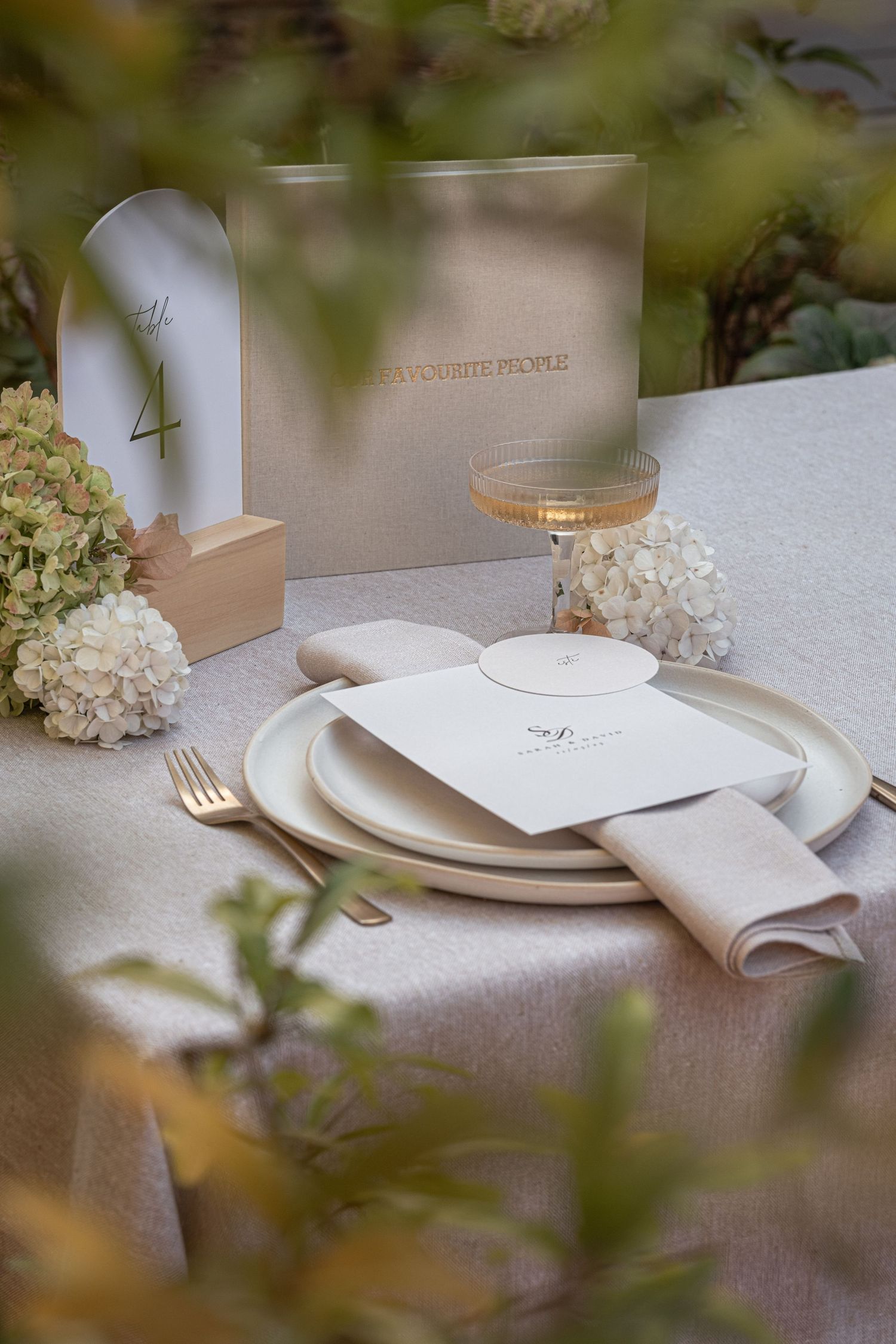 Elegant outdoor wedding table setting with white hydrangeas, gold cutlery and champagne coupe glass.