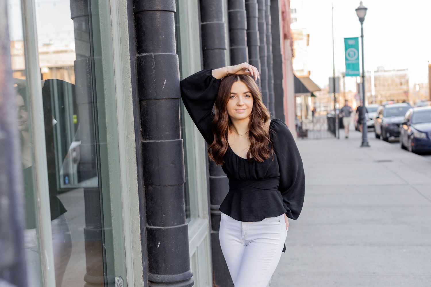 A person in a white sweater and light jeans stands casually on metal stairs against a brick building exterior.