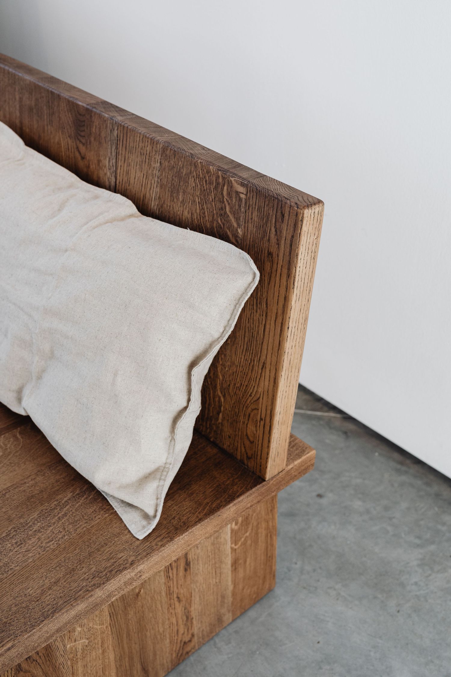 Close-up of rustic wooden bed headboard with linen pillow against white wall.