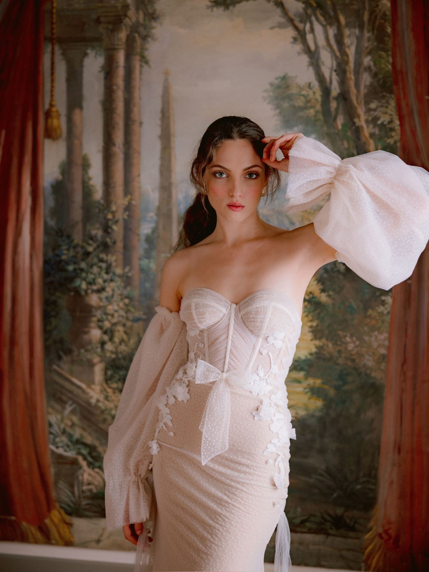 Elegant off-shoulder wedding dress with corset bodice, billowing long sleeves and scenic garden backdrop in romantic setting.
