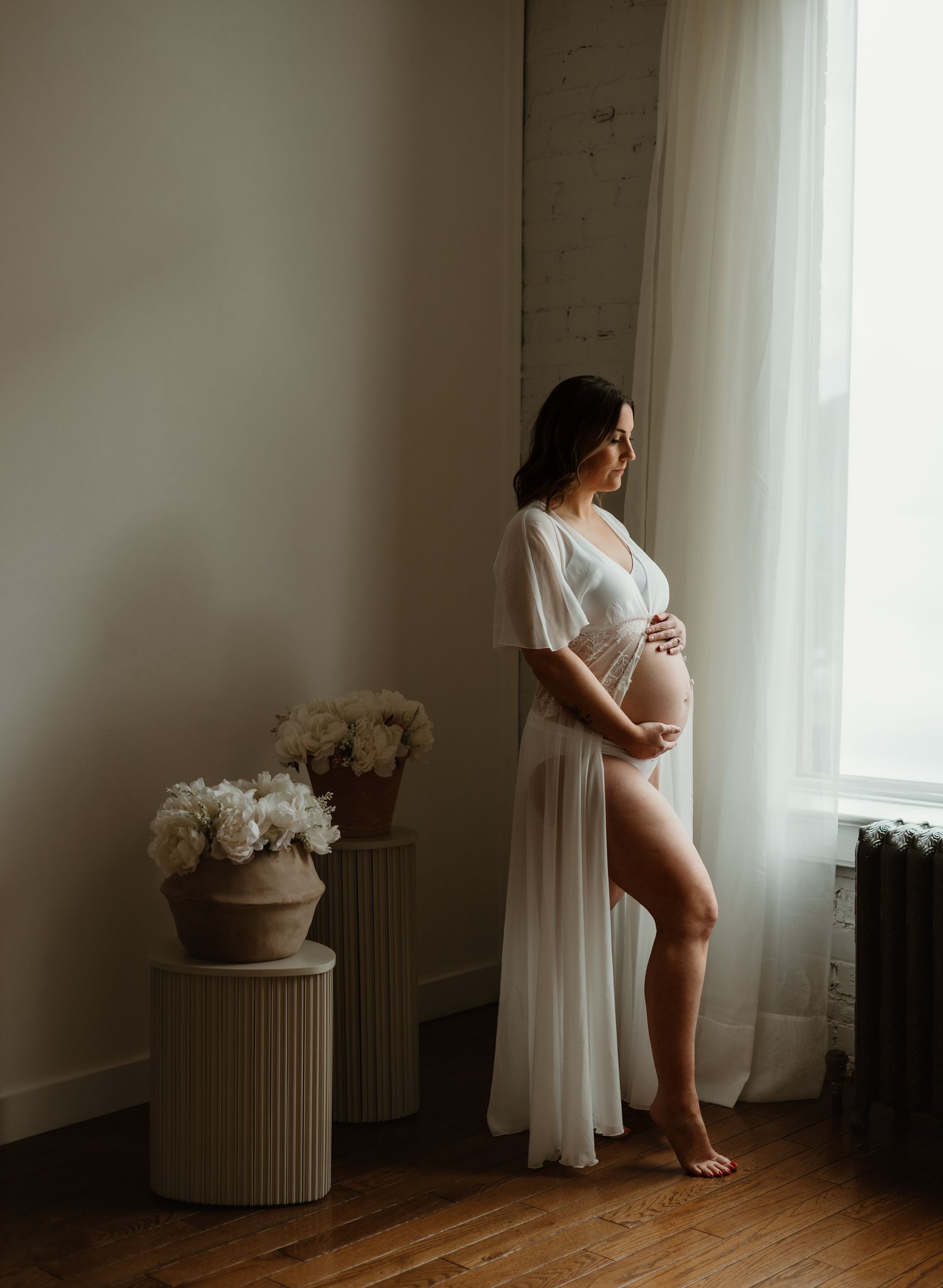 Expecting mother in flowing dress standing in sunlit studio near Calgary