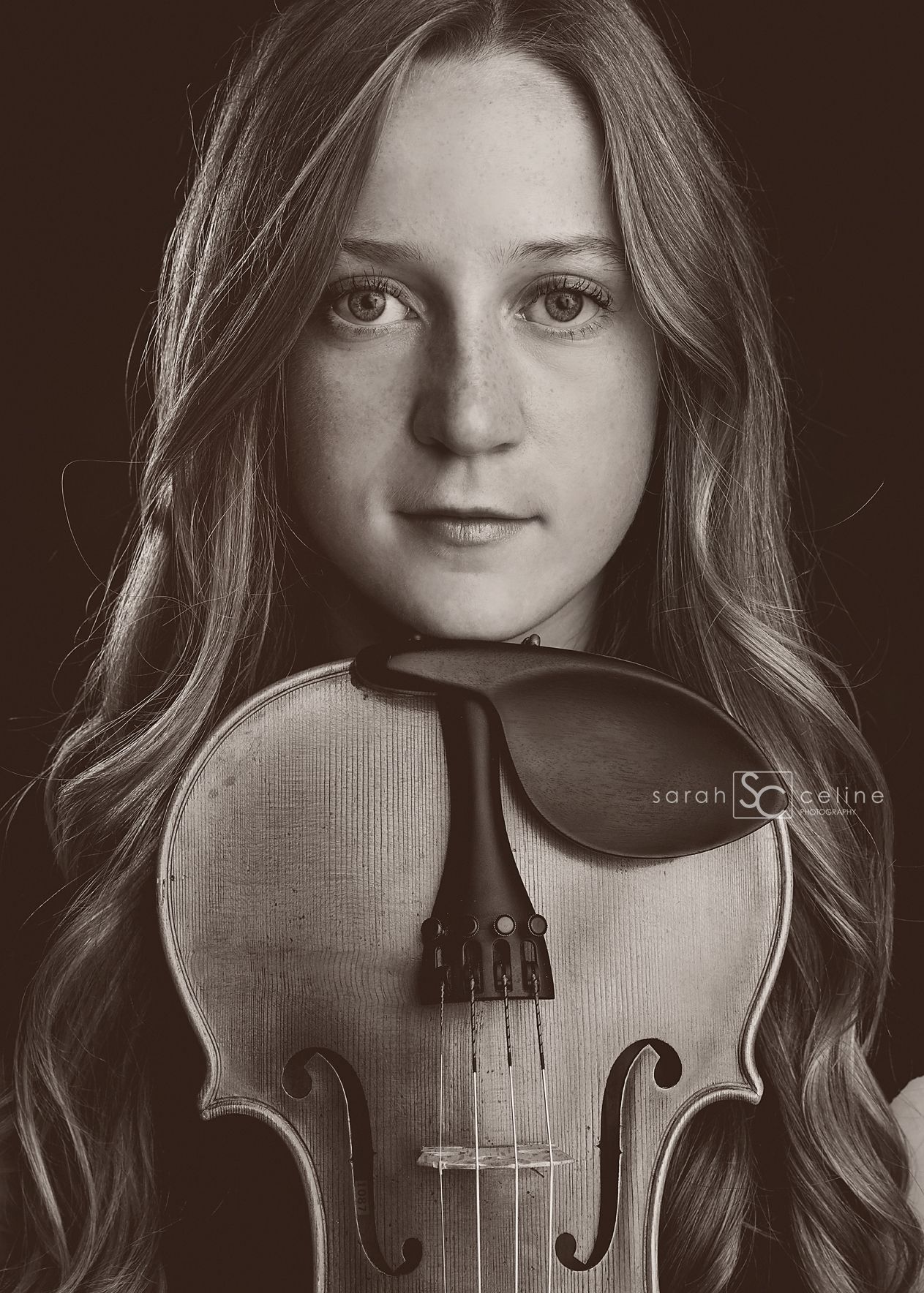A dramatic black and white portrait shows long-haired violinist posing with their instrument in an artistic composition.