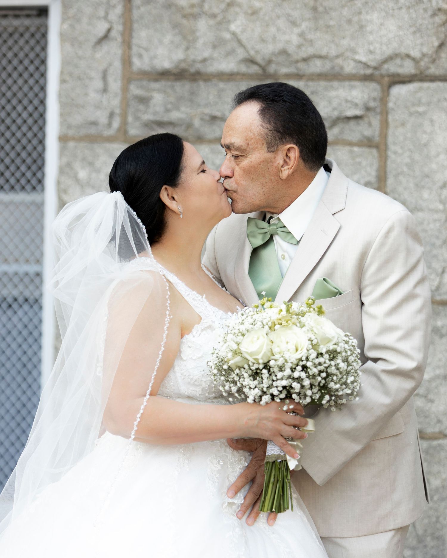 A romantic wedding series showing a couple in a white dress and beige suit embracing while holding a lily of the valley bouquet.