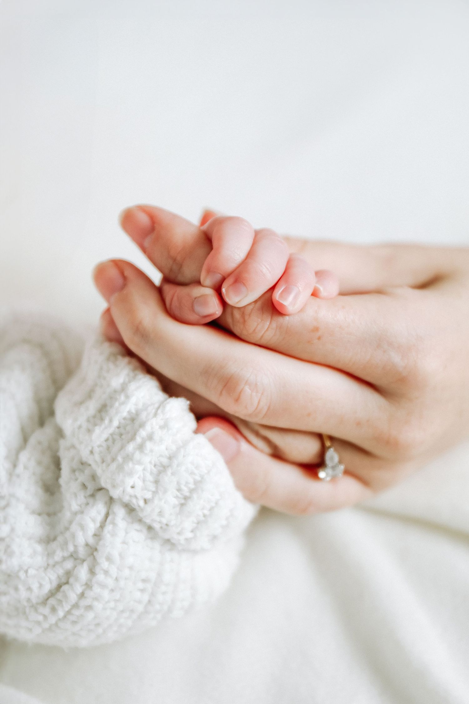 Two hands gently touching against a soft white background creating a delicate and intimate moment, during newborn photoshoot in Nottingham
