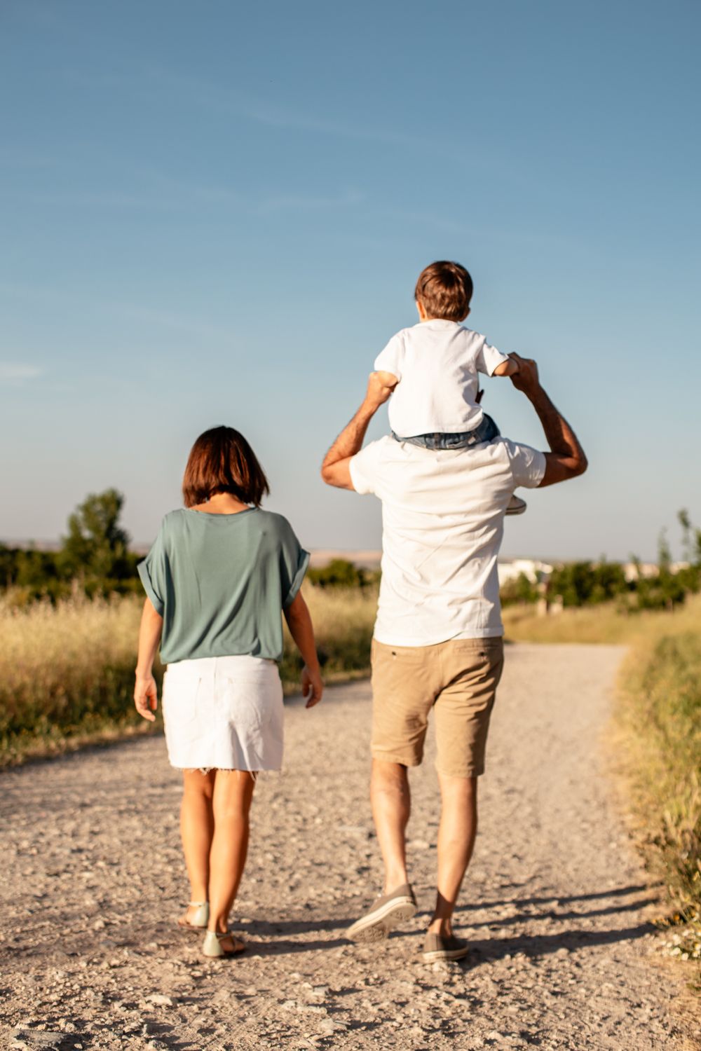 A family walks together on a dirt path during golden hour with a child riding on shoulders.