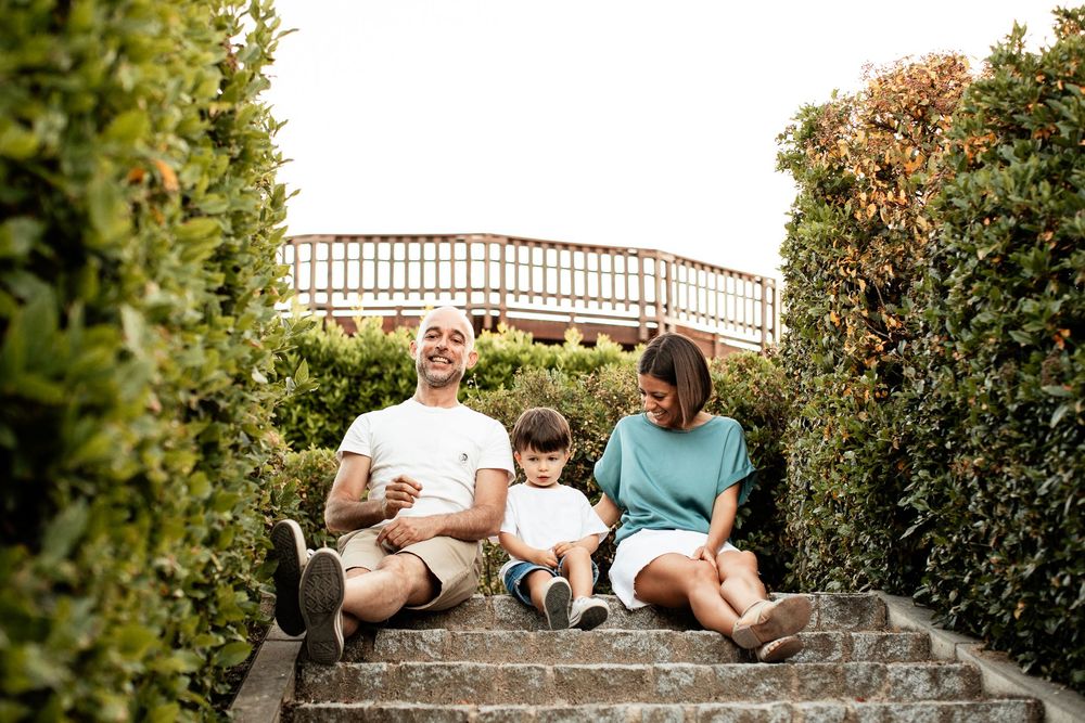 Family relaxing together on stone steps with bridge visible in background.