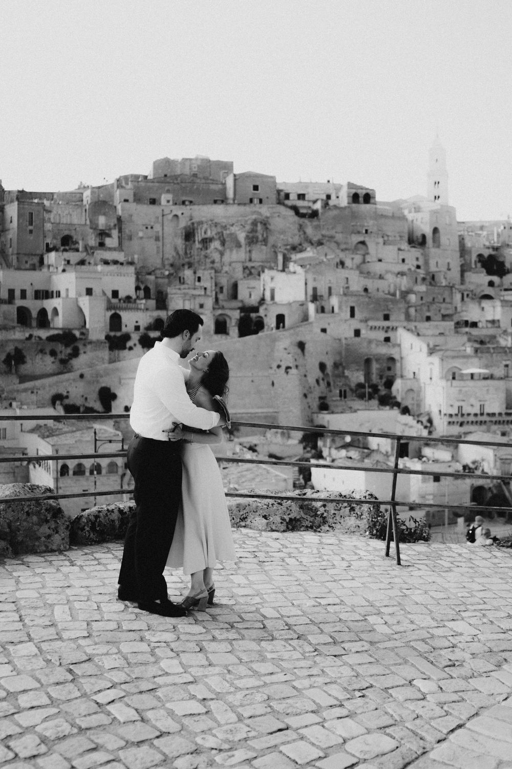 A couple admires the ancient city of Matera from a panoramic stone terrace overlooking the historic Sassi district.