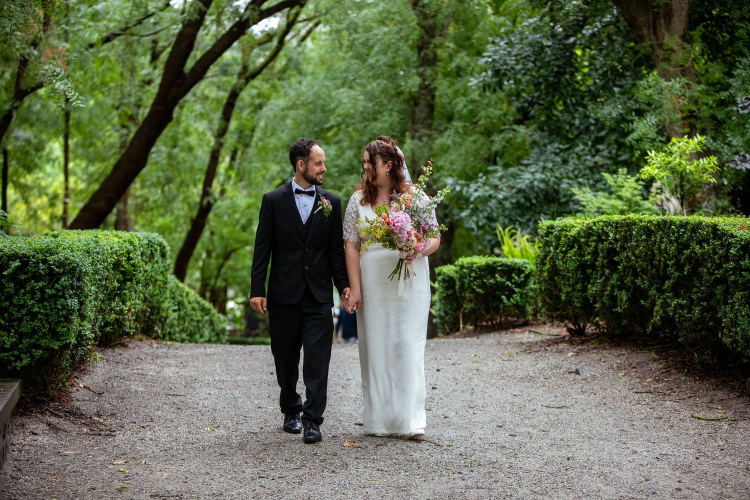 Wedding couple gazing into eyes, walking in lush Melbourne gardens.
