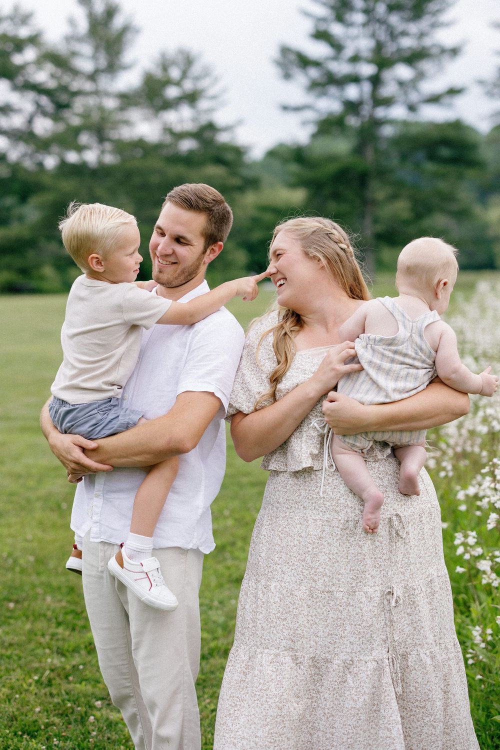 A tender family moment captured outdoors with two small children and parents in white and neutral toned clothing.