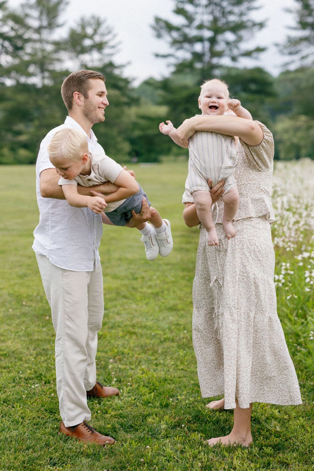 A happy family moment outdoors with twin babies in a field of wildflowers on a sunny summer day.