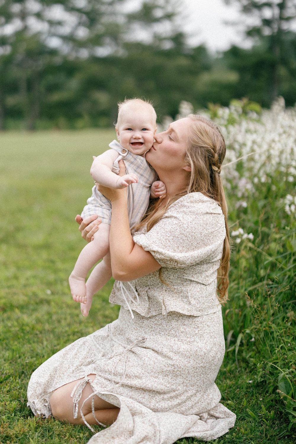 A tender moment shared between parent and baby in a flowery field while wearing light-colored dresses.