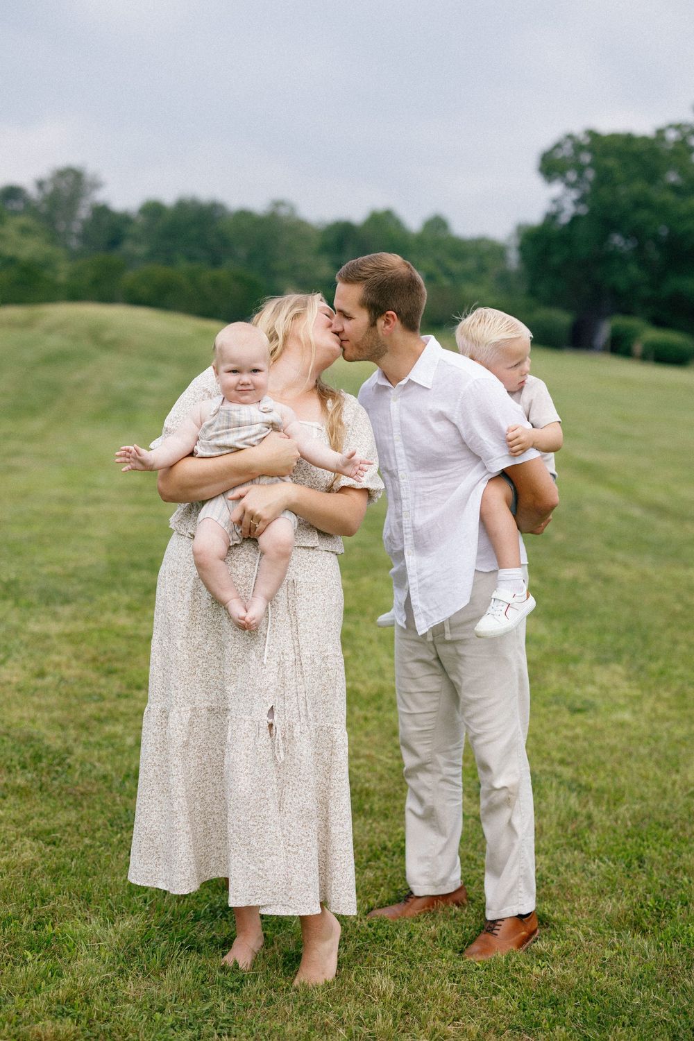 Family photo series showing tender moments together on a grassy hillside in coordinated neutral outfits.