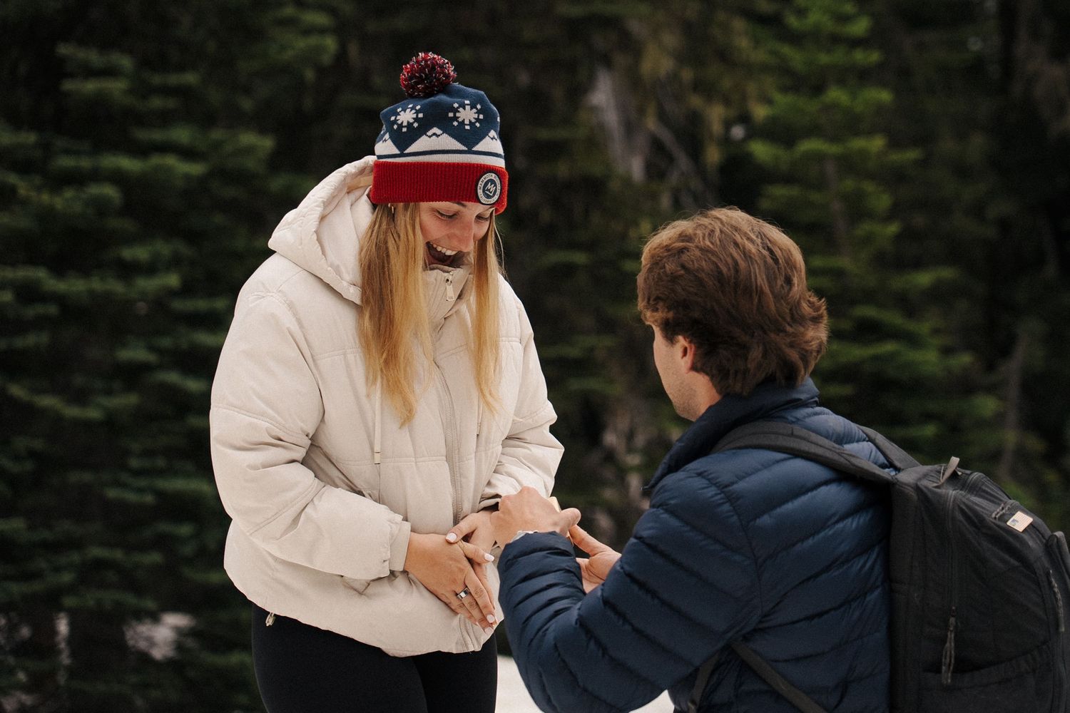 A romantic marriage proposal scene in a snowy winter forest during sunset with evergreen trees in the background.