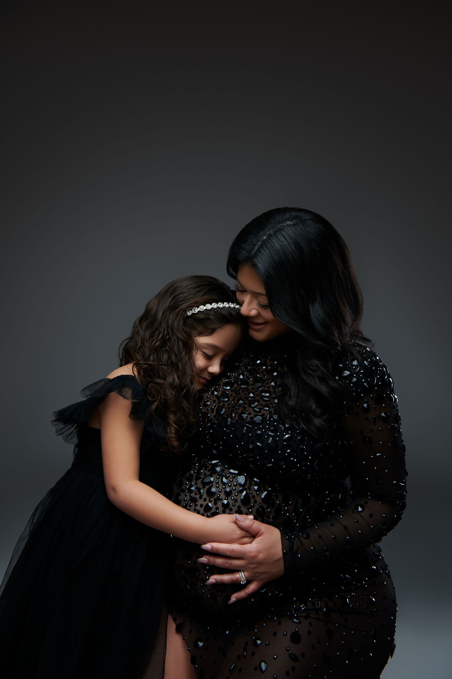 Intimate maternity moment captured with mother and daughter embracing in elegant black dresses. Nutley, NJ Luxury Maternity Photographer
