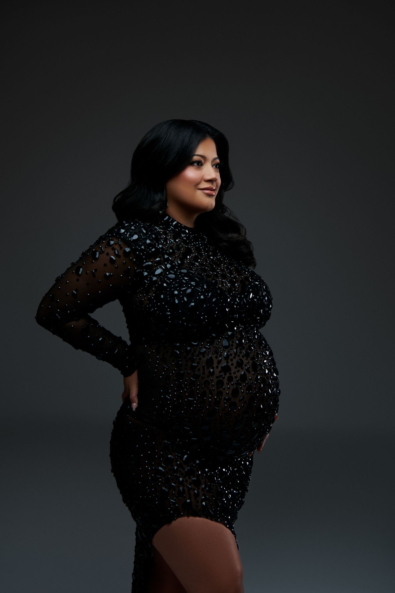 Side view of expectant mother posing in glamorous black sequined dress against dark background. NJ Luxury Maternity Photographer