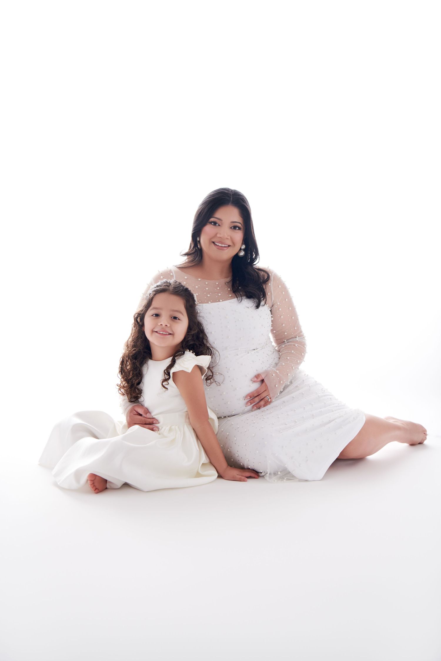A tender maternity studio portrait with white dresses against bright background. Nutley NJ Luxury Maternity Photographer